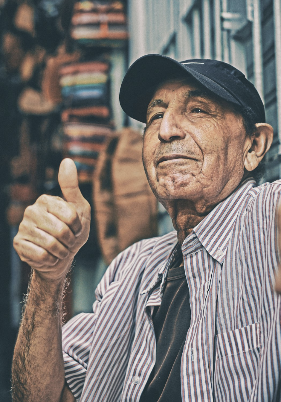 An elderly man wearing a cap gives a thumbs-up with a confident expression, symbolizing positivity and appreciation
