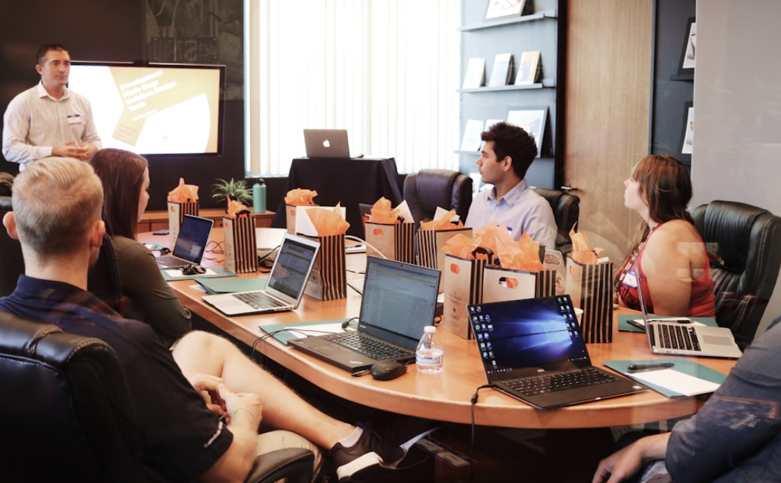 Riunione di lavoro con un gruppo di professionisti seduti attorno a un tavolo da conferenza, impegnati in una discussione con un relatore che conduce la sessione.